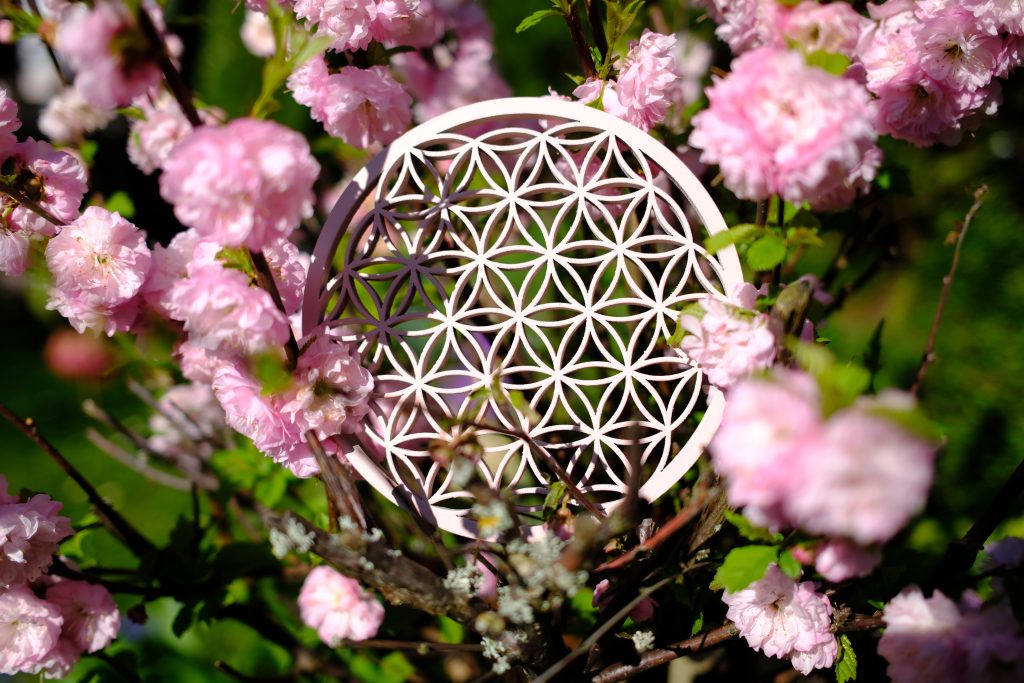 Makroaufnahme einer Blume des Lebens Skulptur vor einem rosafarbenen Blumenstrauch